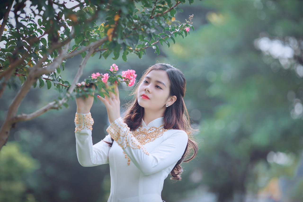 About An elegant woman in traditional Ao Dai appreciating the beauty of pink blossoms.