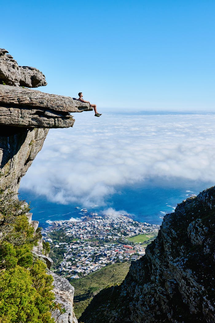 Home A person sits on a cliff edge enjoying a breathtaking view of the ocean and city below.